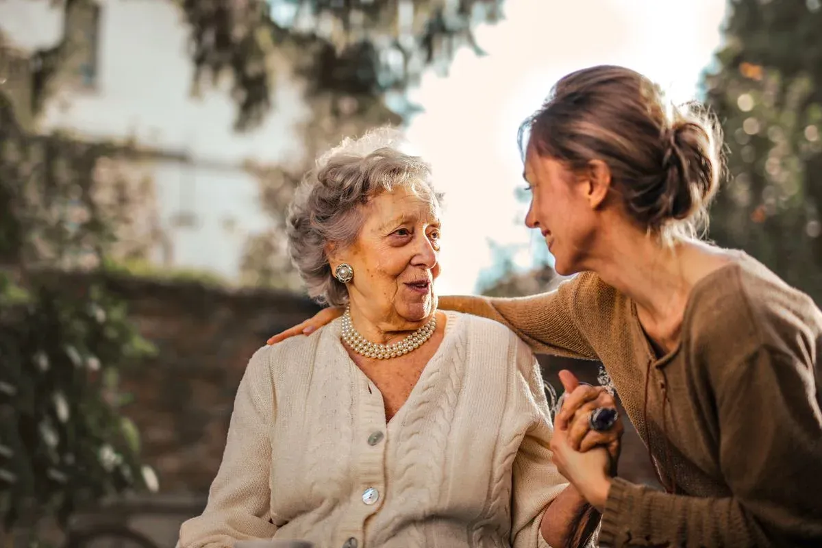 An older woman in conversation with a younger woman, sitting together outdoors.