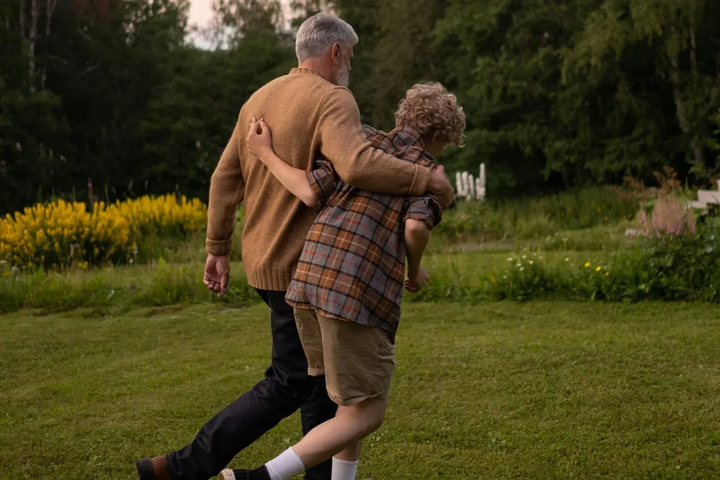 A grandfather and his grandson walking a garden path together, arm in arm.